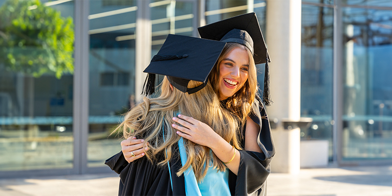 Two students in graduation attire in a hugging embrace